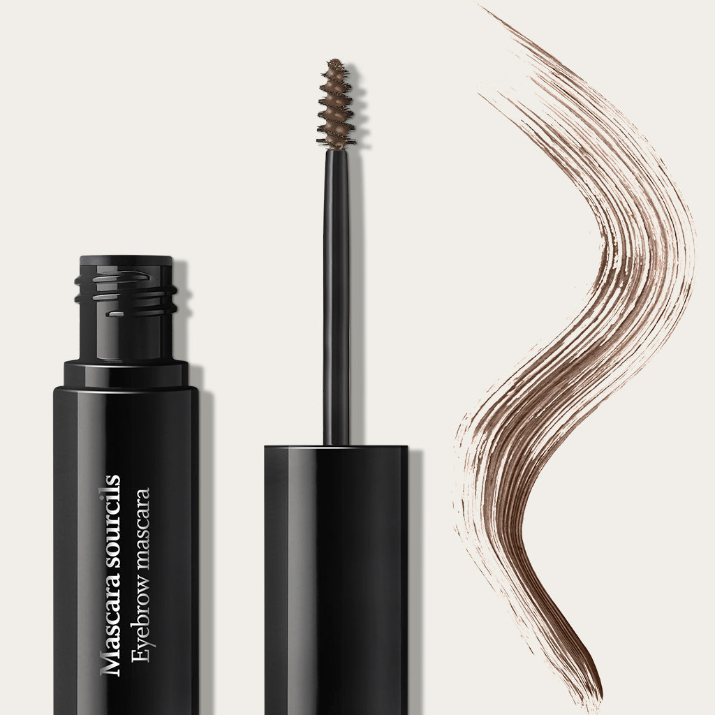 Open black tube of mascara sourcils with spoolie wand and brown eyebrow mascara stroke on beige background